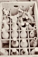 A wooden box of vintage glass bottles; some are worn or chipped, while others are completely broken apart toward the neck.